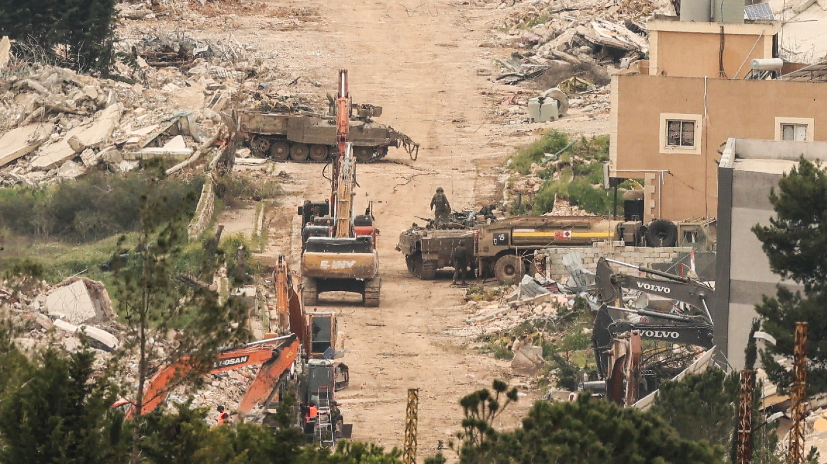 A photo taken from the Israeli side of the border with Lebanon shows Israeli army armoured vehicles and excavators on a road running along destroyed buildings in south Lebanon on 15 April 2026 (AFP)