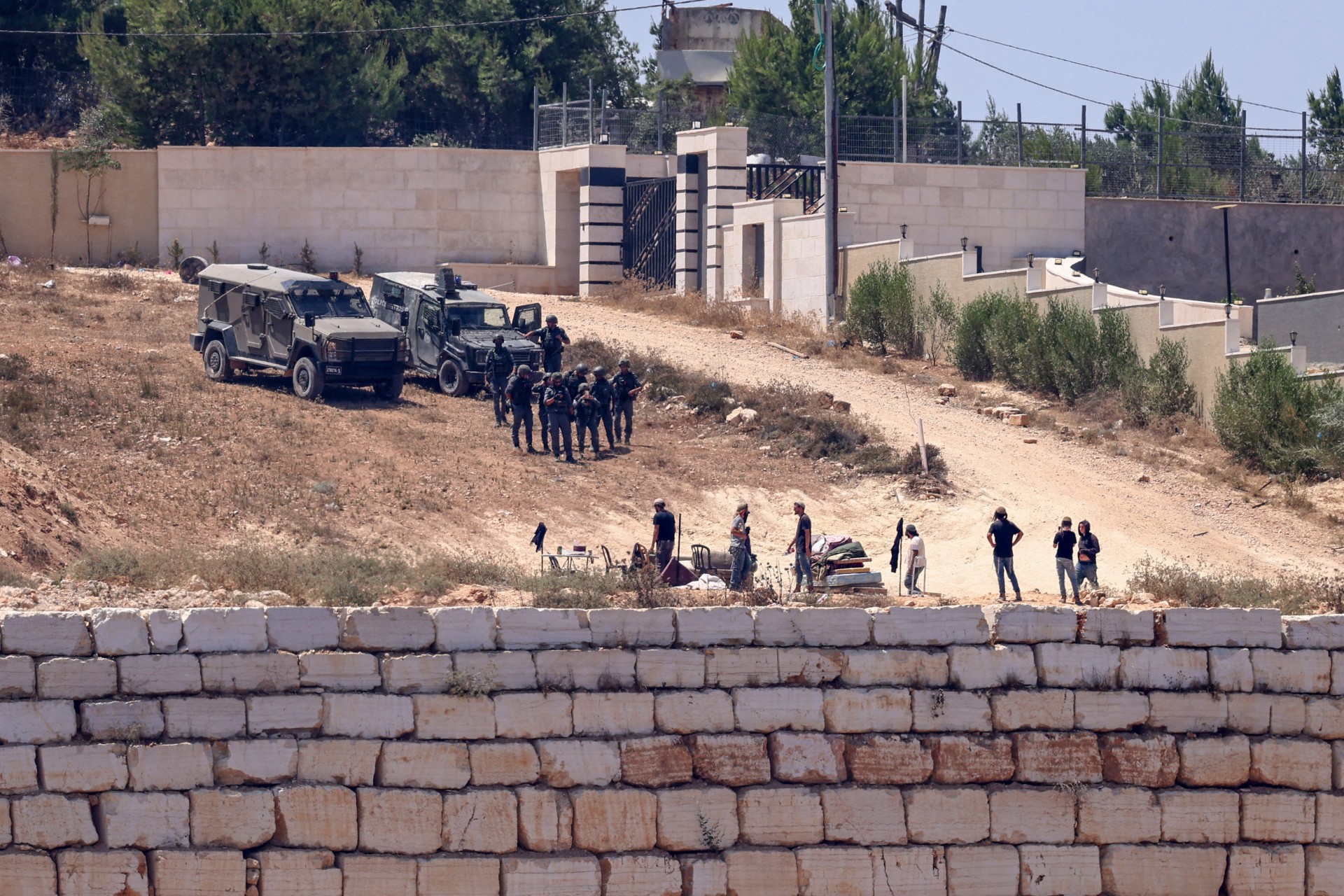 Israeli soldiers (top) stand guard next to settlers in front of the Palestinian houses in the village of Qusra in the occupied West Bank, on 12 August 2026 (Zain Jaafar/AFP)