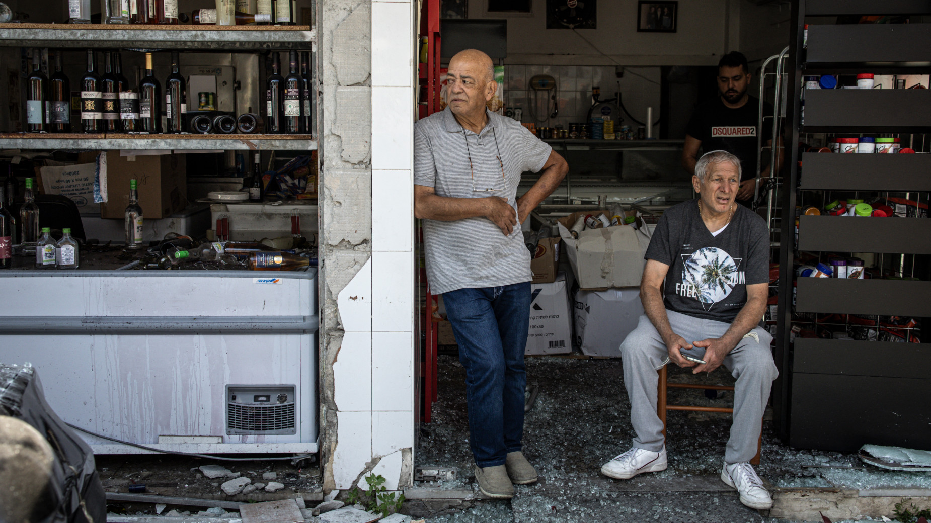 Men sit at the entrance to their damaged shop, following an overnight Iranian missile strike in Bat Yam on 15 June 2025 (AFP)