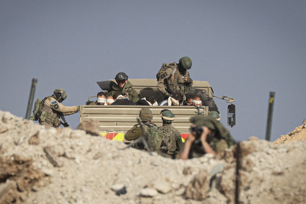 Israeli soldiers detain blindfolded Palestinian men in a military truck while watching Palestinians (not pictured) fleeing the fighting in war-torn Gaza walk by on a road in the Zeitoun district of the southern part of the Gaza Strip on November 19, 2023