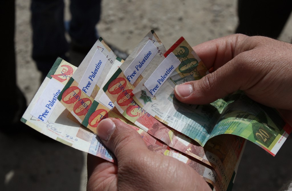 Israeli shekels are seen marked with ‘Free Palestine’ stickers in 2011 (AFP)