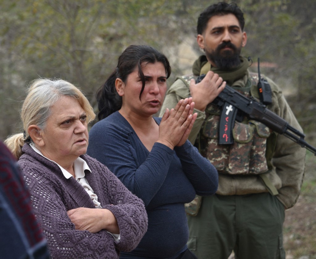 Women stand by a volunteer villager wearing a camouflage army outfit and holding a Kalashnikov rifle patroling in the village of Zabux near the Lachin corridor on November 26, 2020, after six weeks of fighting between Armenia and Azerbaijan over the disputed Nagorno-Karabakh region.