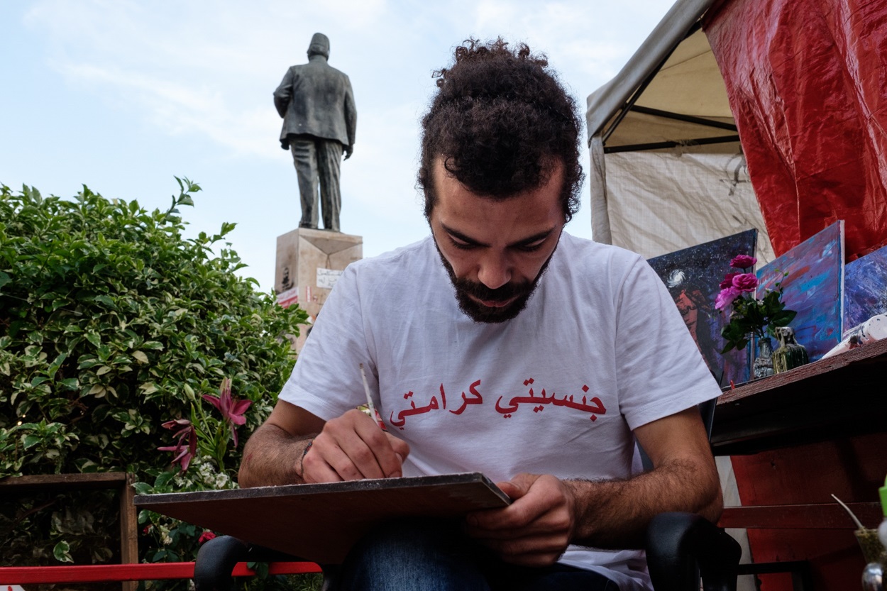 Mahmoud al Khash, better known as Abou Ward, near the sign he painted for the 'Jinseeyati Kaamity' - 'My Nationality, My Dignity' - tent (MEE/Rita Kabalan)