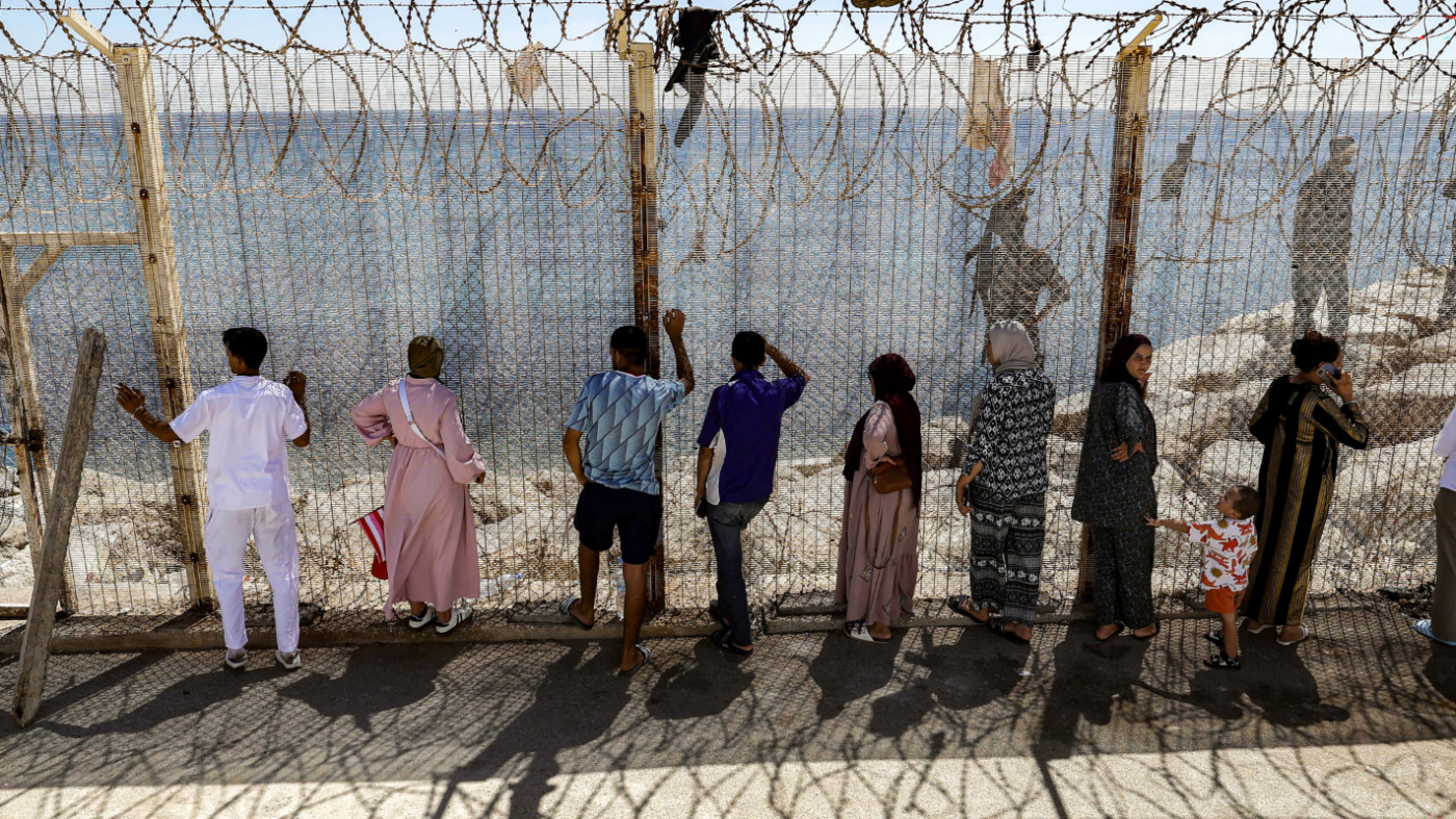 Relatives wait by a fence for the return of people who had previously crossed into Spain's North African enclave of Ceuta, at Morocco's Bab Sebta border crossing on 2 August 2026 (AFP)