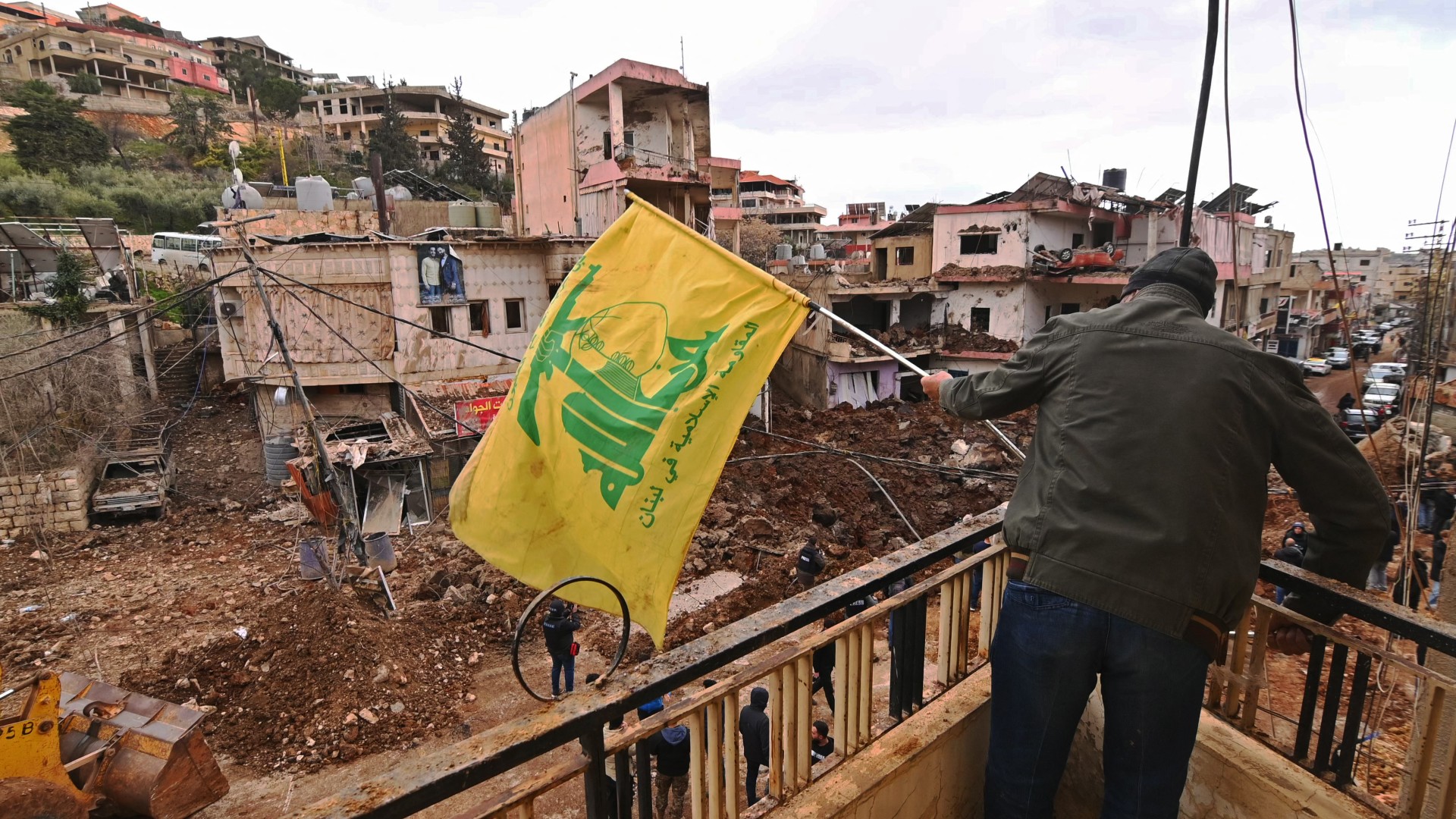 A man installing a Hezbollah flag on the balcony of a damaged building in Nabi Sheet after an Israeli military attack in the Bekaa Valley, on 7 March 2026 (Fadel Itani/AFP)