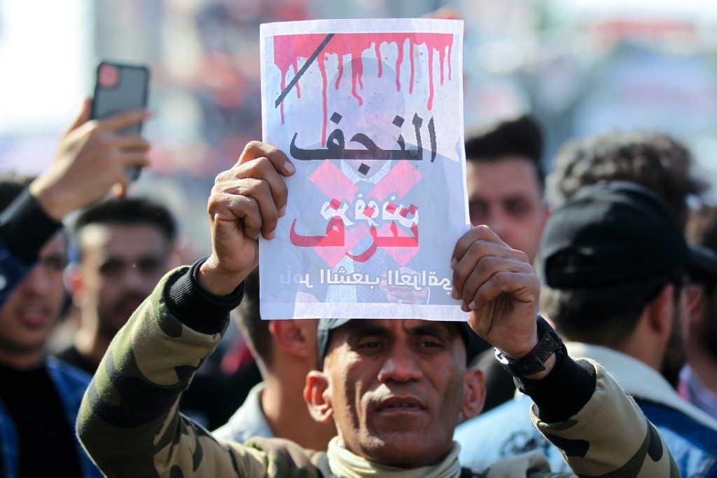 An Iraqi protester lifts a placard with the inscription 