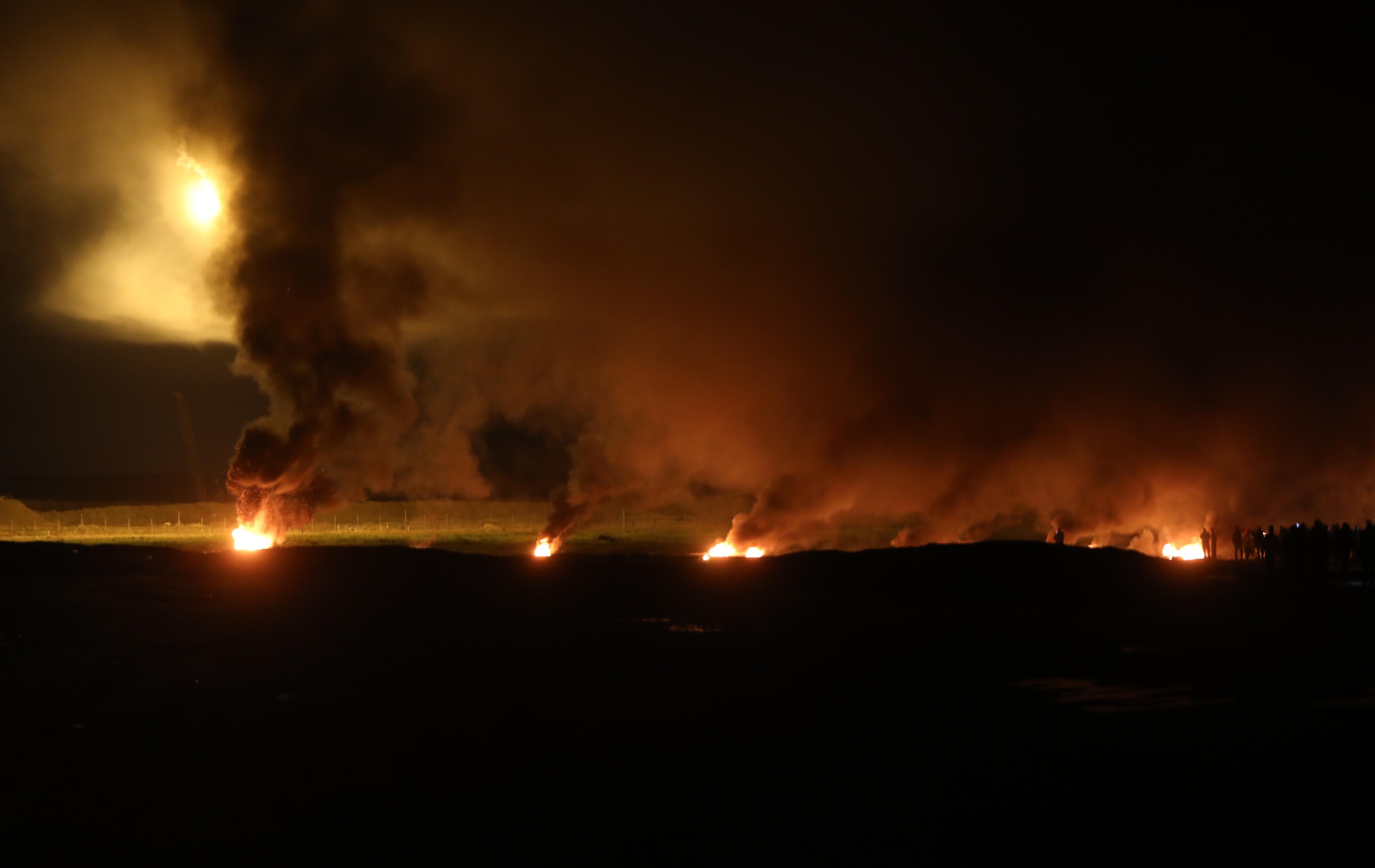 Protesters set tyres on fire along the fence separating Gaza from Israel, while Israeli forces lit flares on 11 February 2019 (MEE/Mohammed Asad)