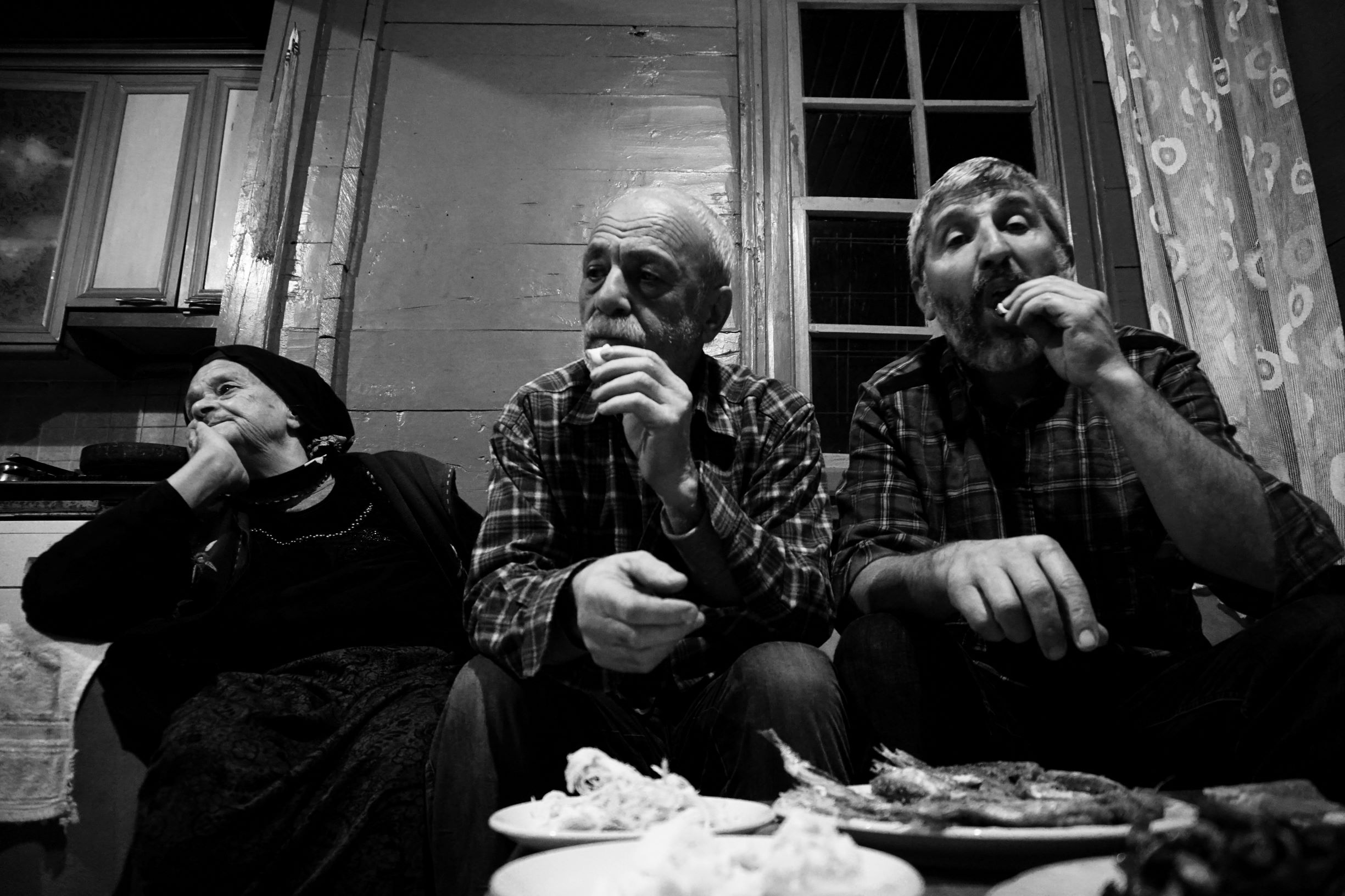 Ms Vaic, her son and Harun Aksu sit and eat the traditional Black Sea food (anchovy, corn bread, black cabbage) and watch the Turkish news (Nimet Kirac / MEE)