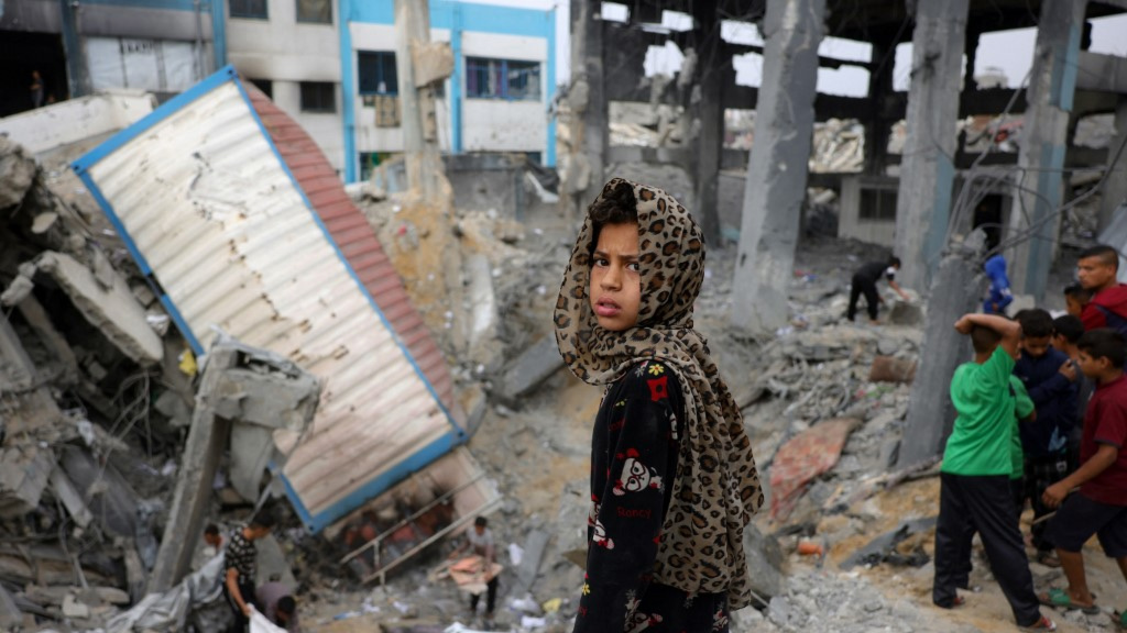 A Palestinian girl looks on as children gather at the rubble of an aid depot damaged in Israeli bombing in Jabalia, Gaza, on 10 May 2025 (Bashar Taleb/AFP)