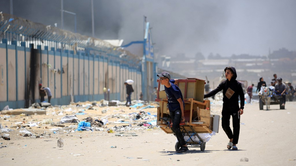 Palestinians flee with their belongings as smoke rises in the background, in the area of Tel al-Sultan in Rafah, Gaza, on 30 May 2024 (Eyad Baba/AFP)