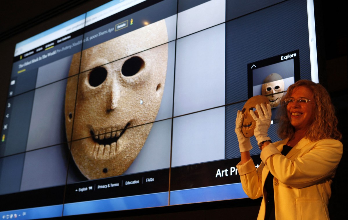 sraeli Museum curator Debby Hershman holds up a Neolithic mask, that is also projected in the background, as part of the Google Art Project in April, 2012 in Jerusalem (AFP)