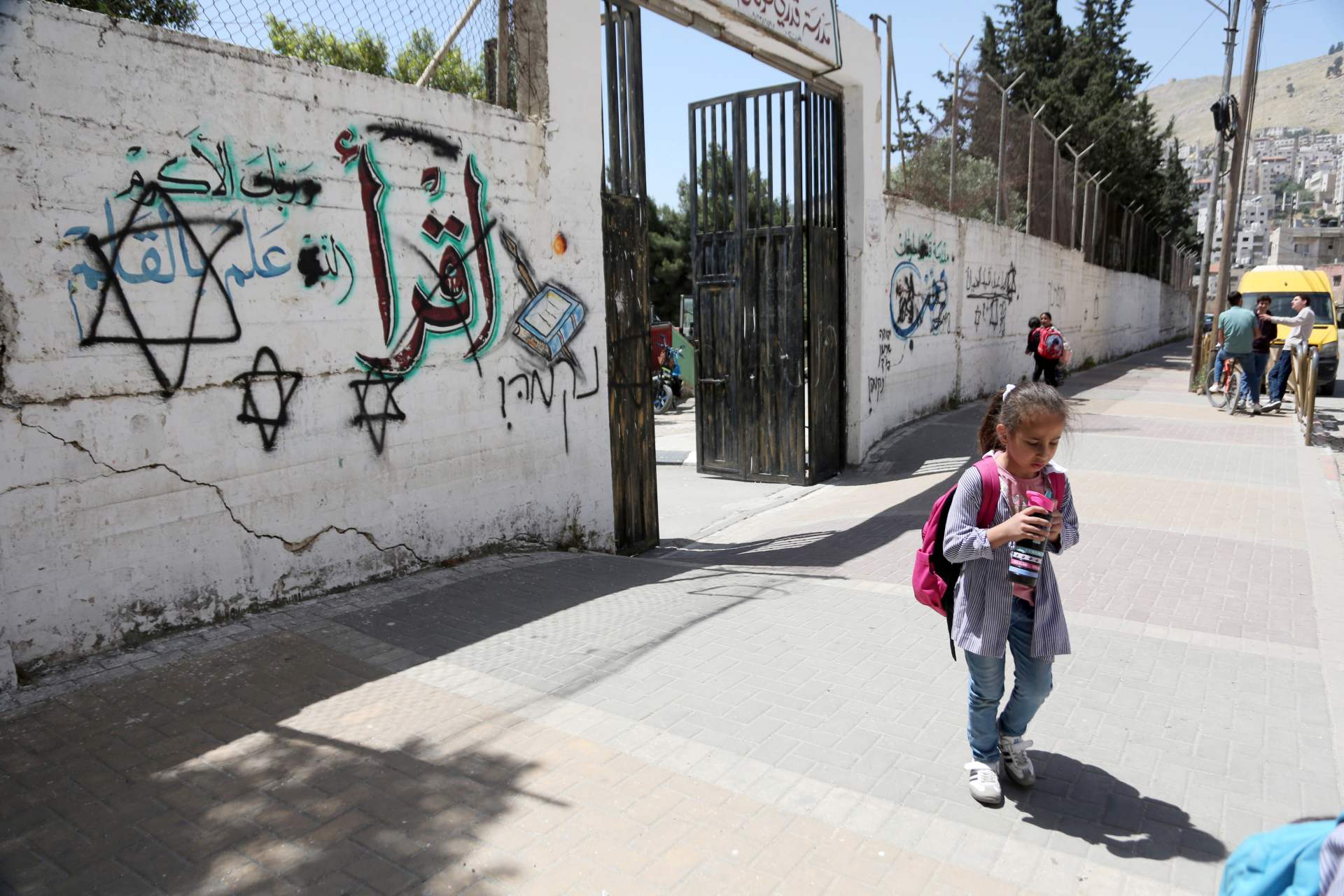 A girl walks past Hebrew graffiti painted by settlers on the wall of a Palestinian school in the West Bank city of Nablus in April 2026 (Reuters)