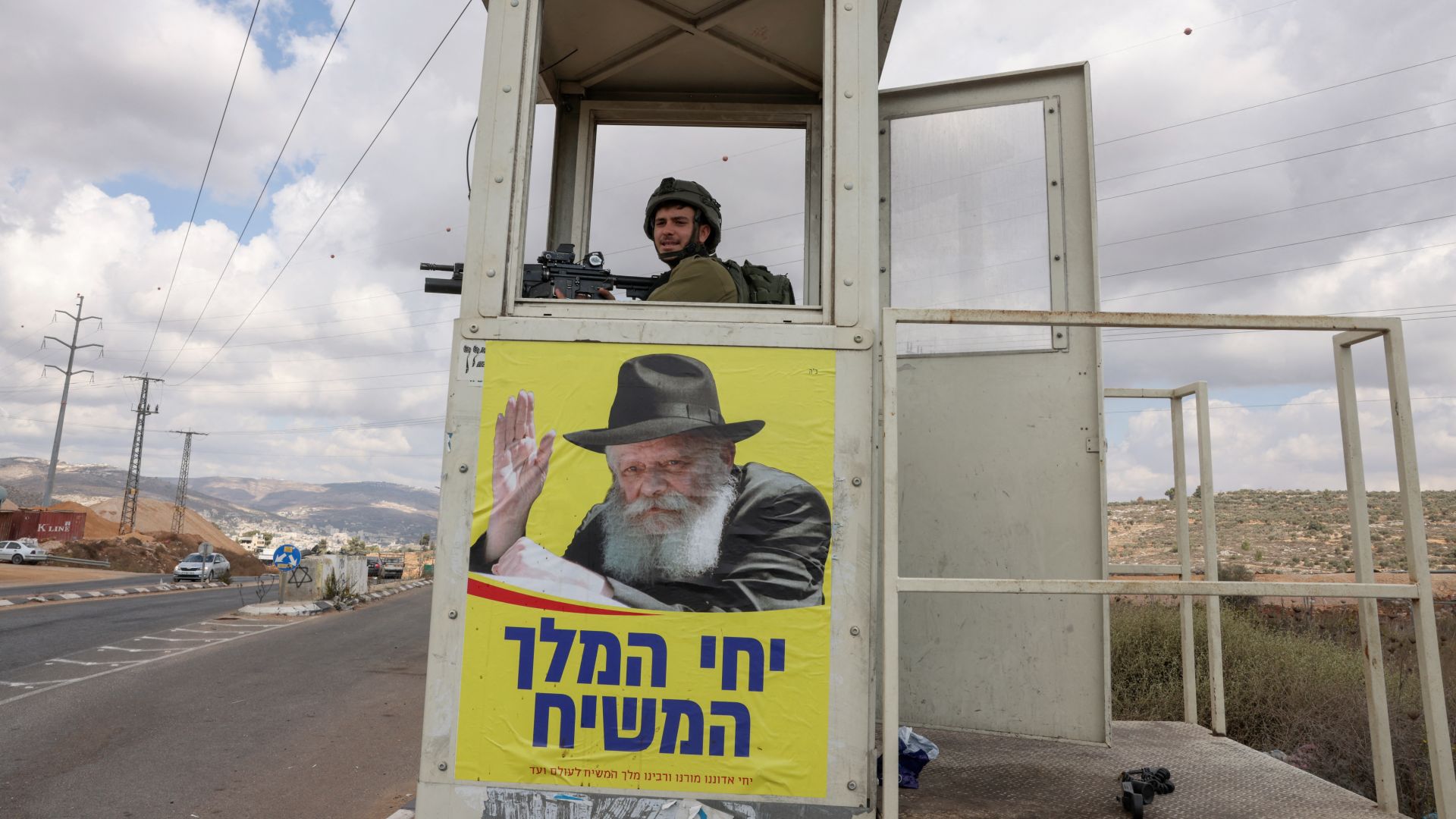 An Israeli soldier at an army post bearing a poster of Rabbi Menachem Mendel Schneerson at a junction south of Nablus in 2021 (Menahem Kahana/AFP)