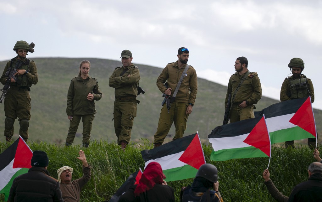 Israeli soldiers stand guard as Palestinians protest against the annexation of the Jordan Valley on 29 February (AFP)
