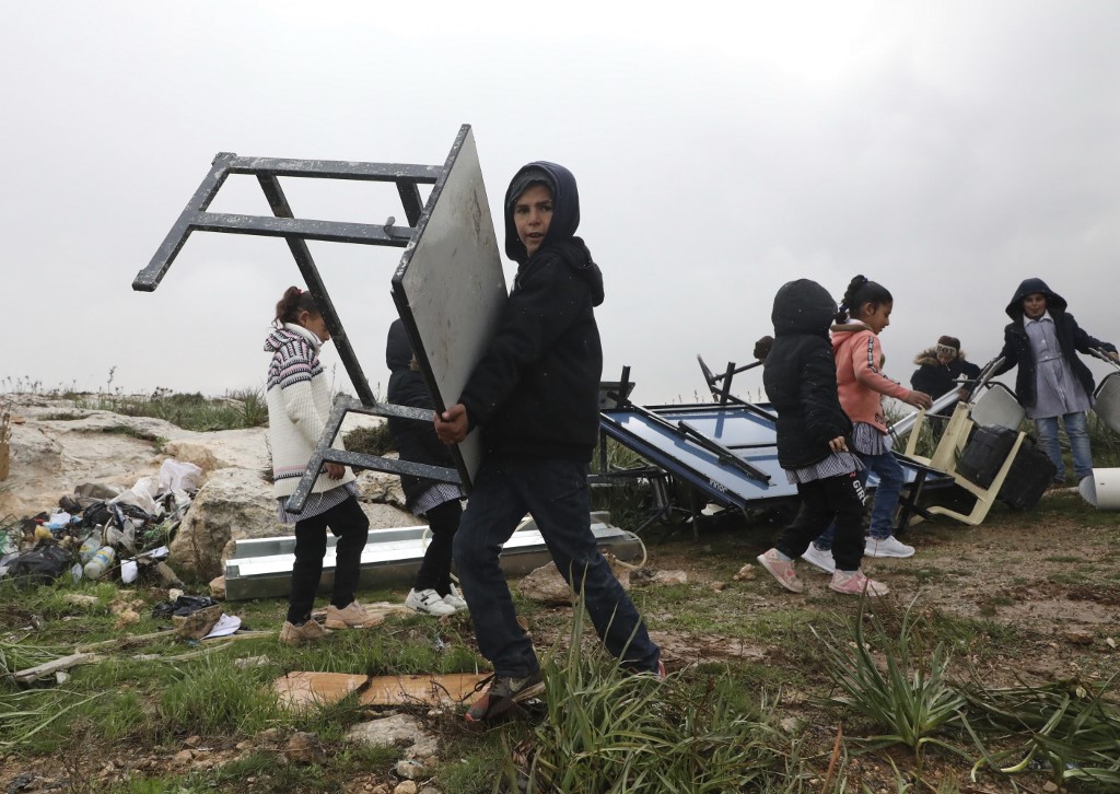 Palestinian children move their classroom furniture after Israeli forces dismantled a school facility on the outskirts of Hebron in the occupied West Bank on 19 February (AFP)