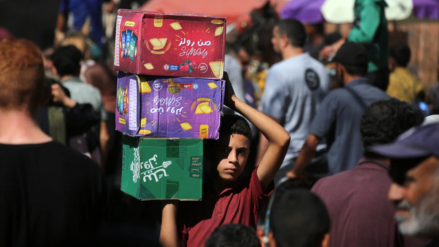 A Palestinian boy carries boxes of biscuits at a market in Deir el-Balah in the central Gaza Strip on 18 October 2025 (AFP)