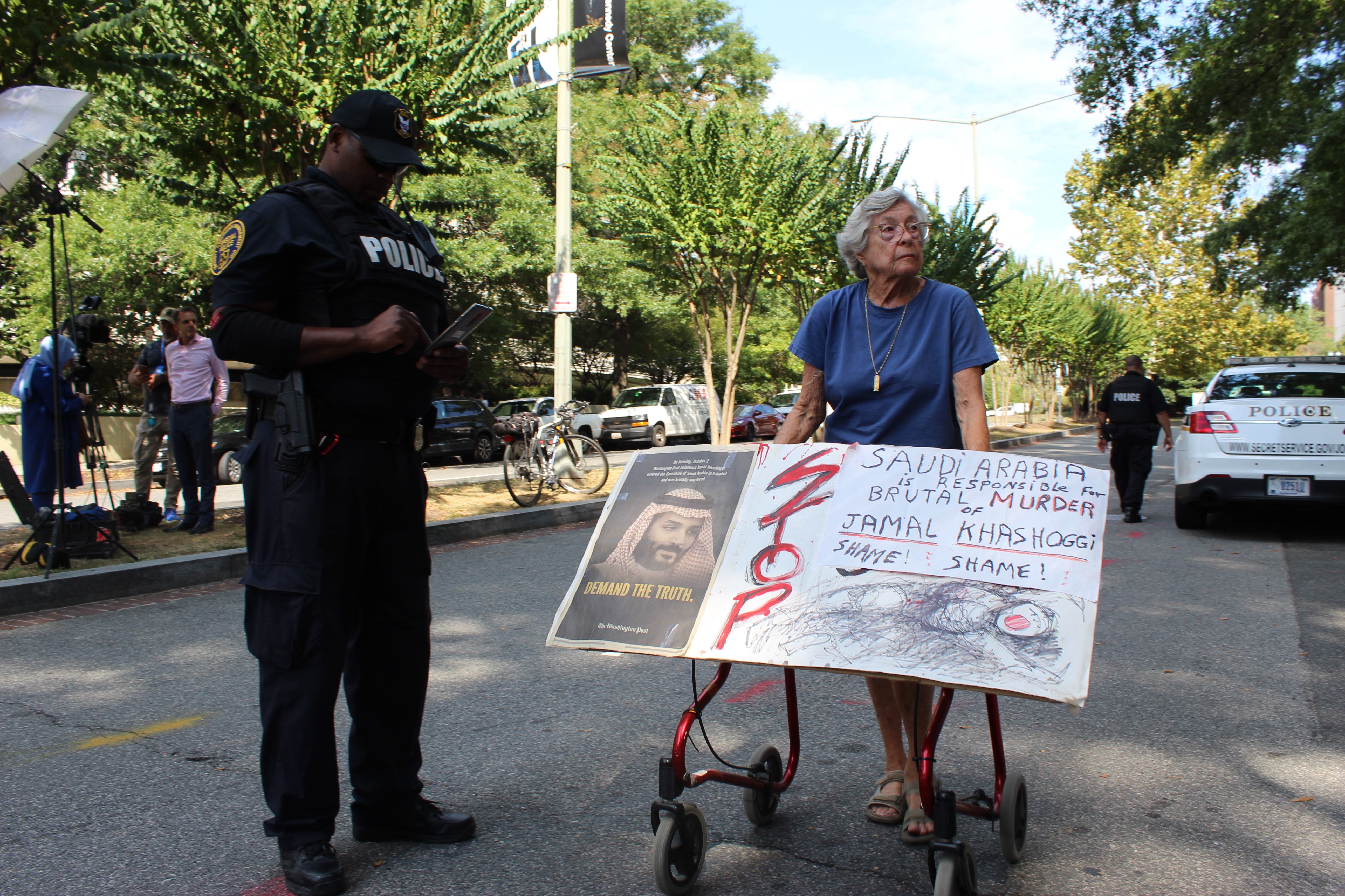 One protester arrives, a sign perched on her walker that reads: 