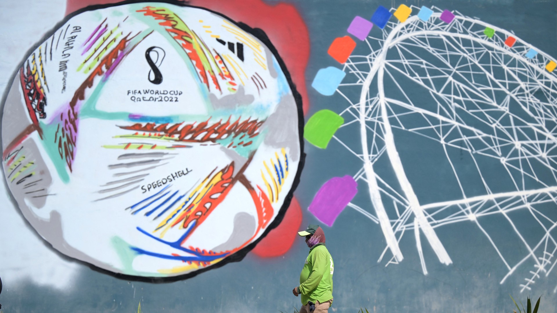 A worker walks past a graffiti along a street in Doha on November 16, 2022, ahead of the Qatar 2022 World Cup football tournament.