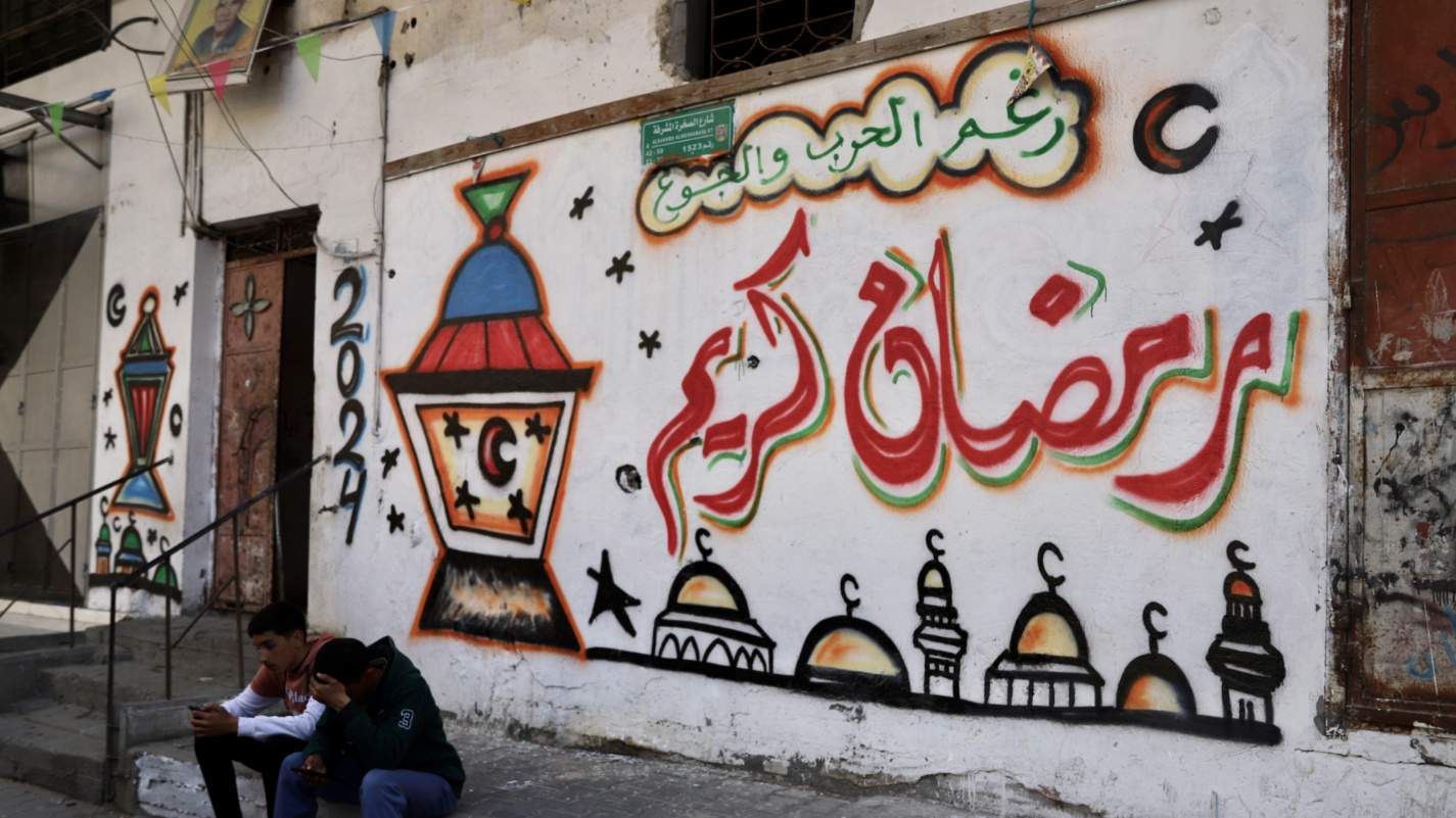 Palestinian men sit in front of a wall in northern Gaza on 11 March 2024 that reads: 