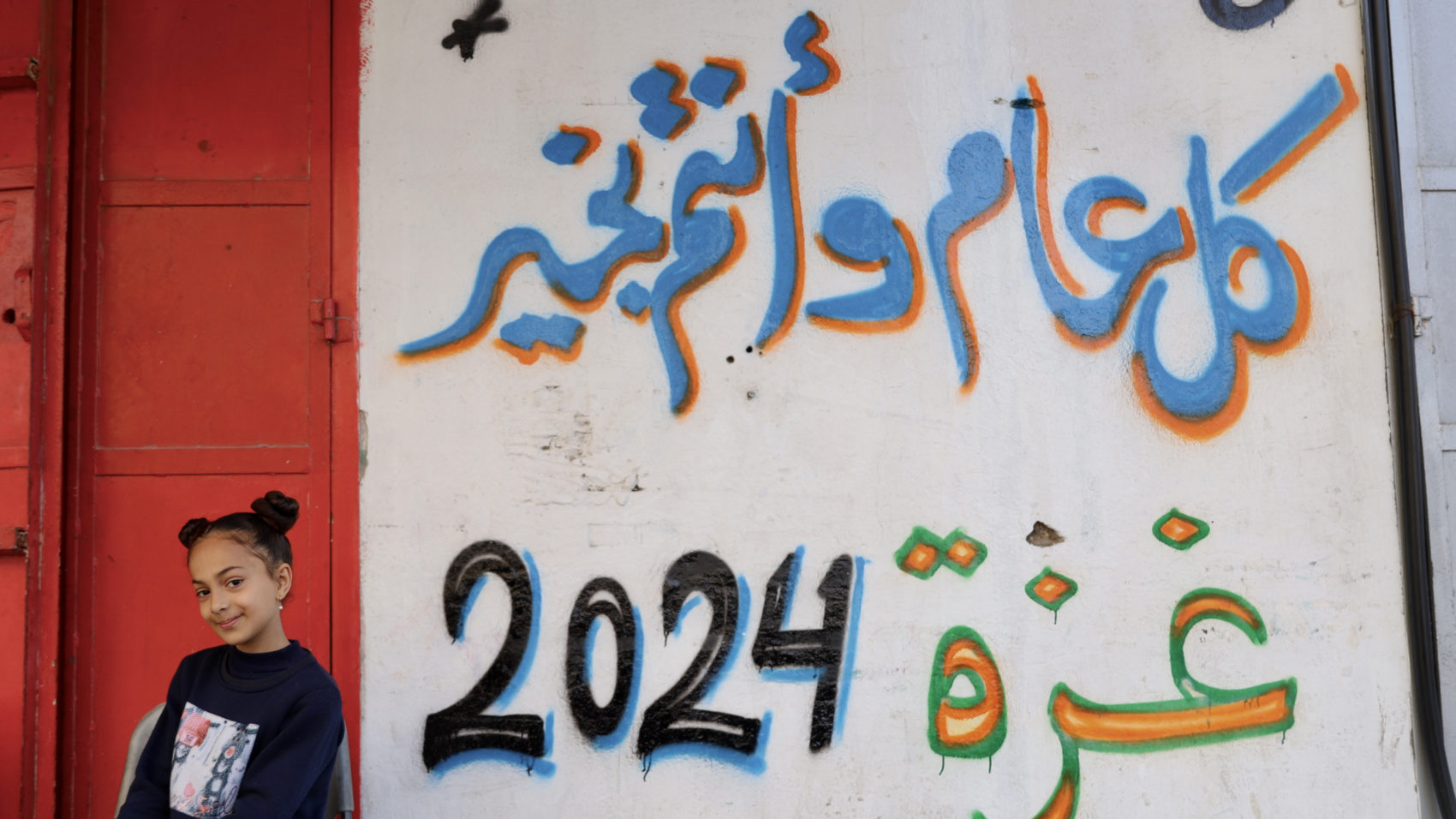 A girl stands in front of a wall painting that reads 