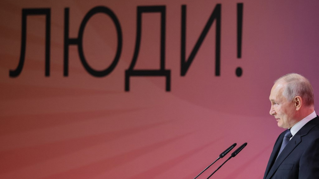 Russian President Vladimir Putin speaks at a forum in Moscow on 29 June 2023, with text next to him reading “People!” (AFP)