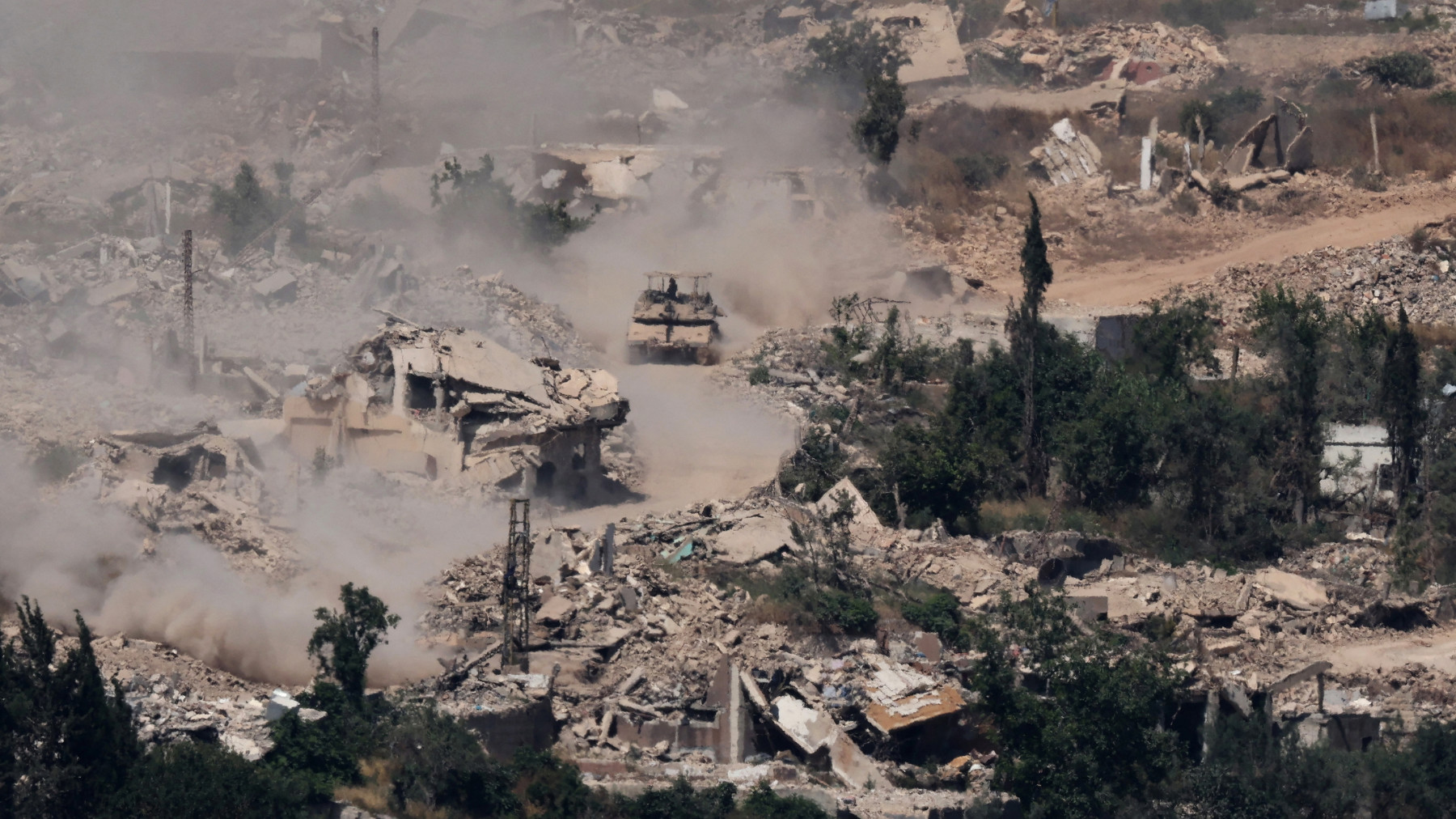 This picture taken from the Upper Galilee in northern Israel, near the border, shows Israeli Merkava tanks driving along a road past destroyed buildings in southern Lebanon on 17 June 2026 (AFP)
