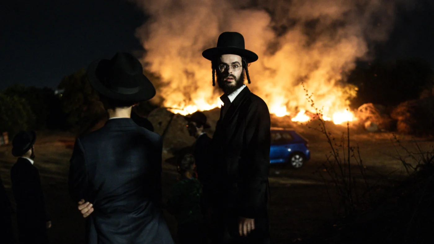 An ultra-Orthodox Jewish man stands in front of a burning fire during a protest against Israeli army conscription in Kfar Yona on 19 August 2025 (AFP)