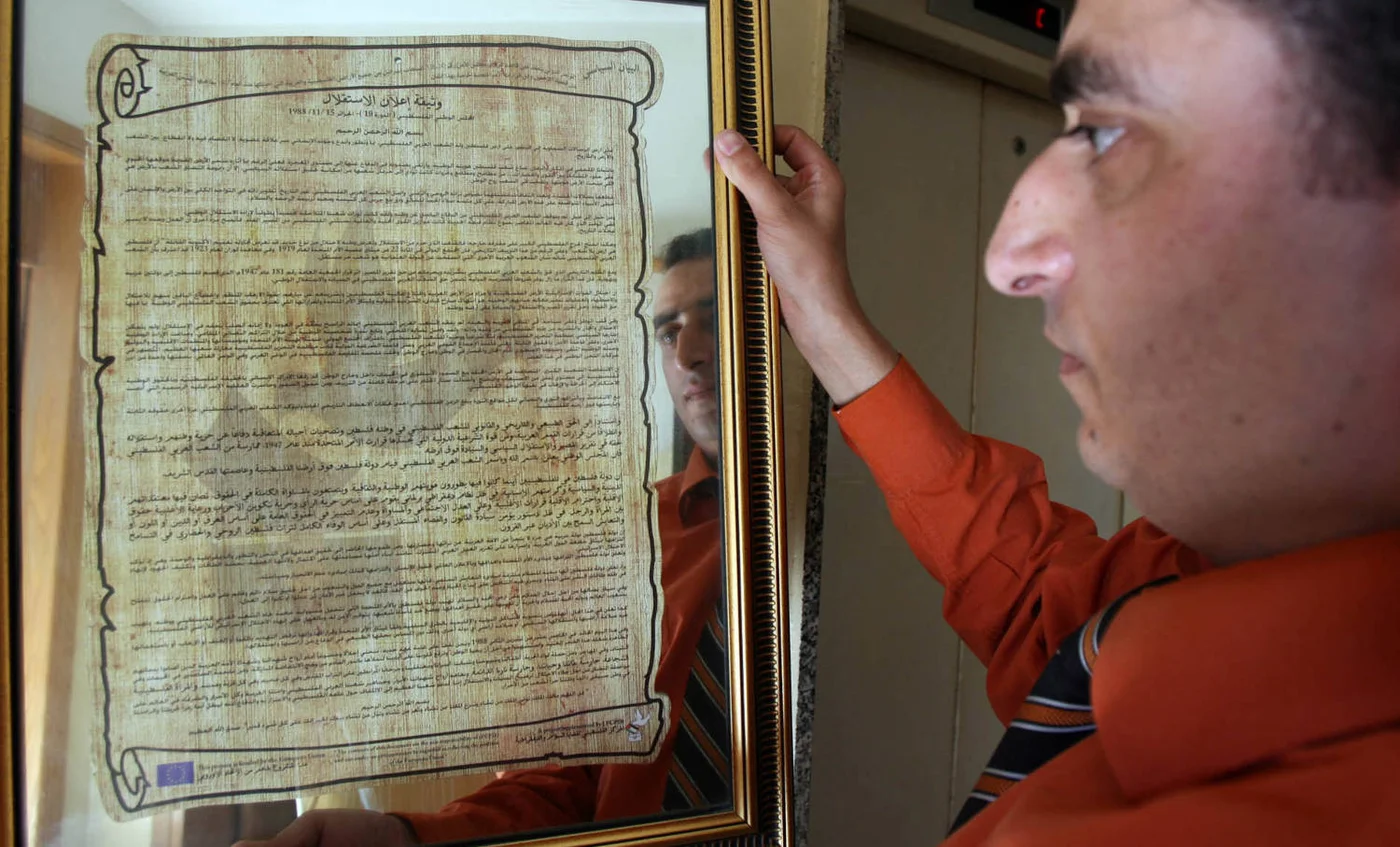A Palestinian man looks at a copy of the Palestinian National Charter of the Declaration of Independence written by Palestinian poet Mahmoud Darwish in Algeria in 1988 (AFP)