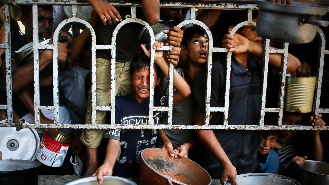 Palestinian children wait for a meal at a charity kitchen in Mawasi, Khan Yunis, southern Gaza on 22 July 2025 (AFP)