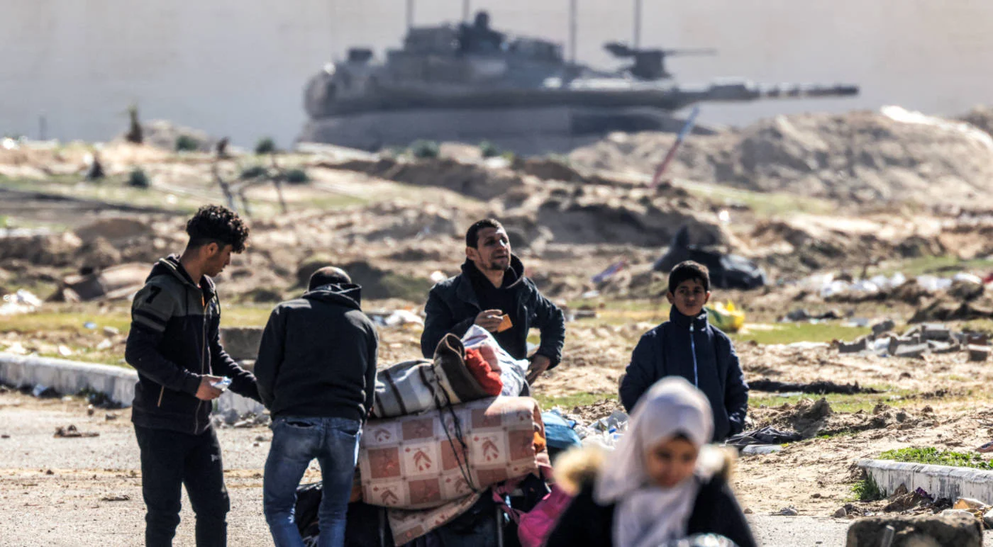 An Israeli battle tank overlooks Palestinian refugees fleeing Khan Yunis, southern Gaza Strip in January 2024 (AFP)