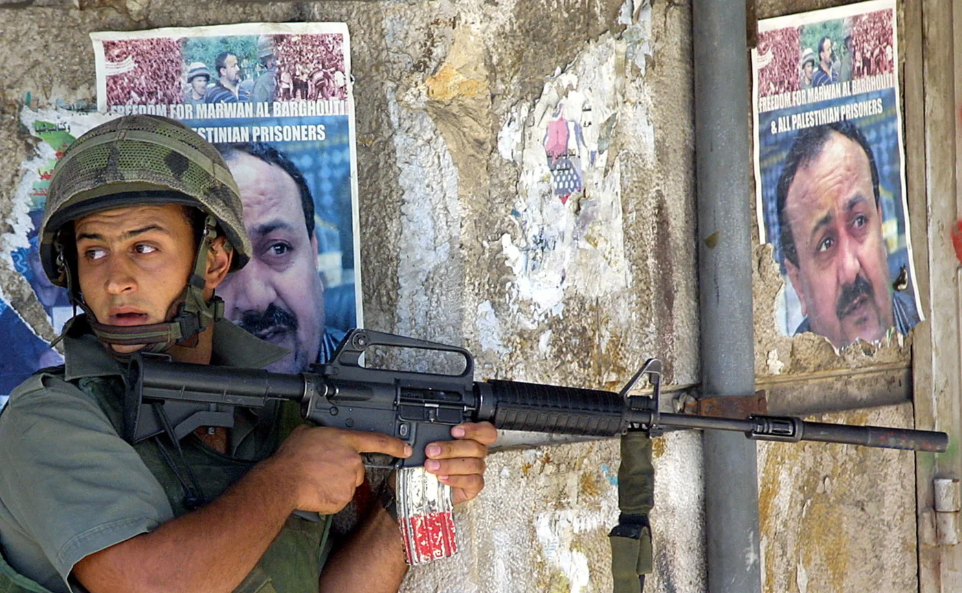 An Israeli border guard next to a wall plastered with pictures of Marwan Barghouti in  Ramallah in  August 2002 (AFP)