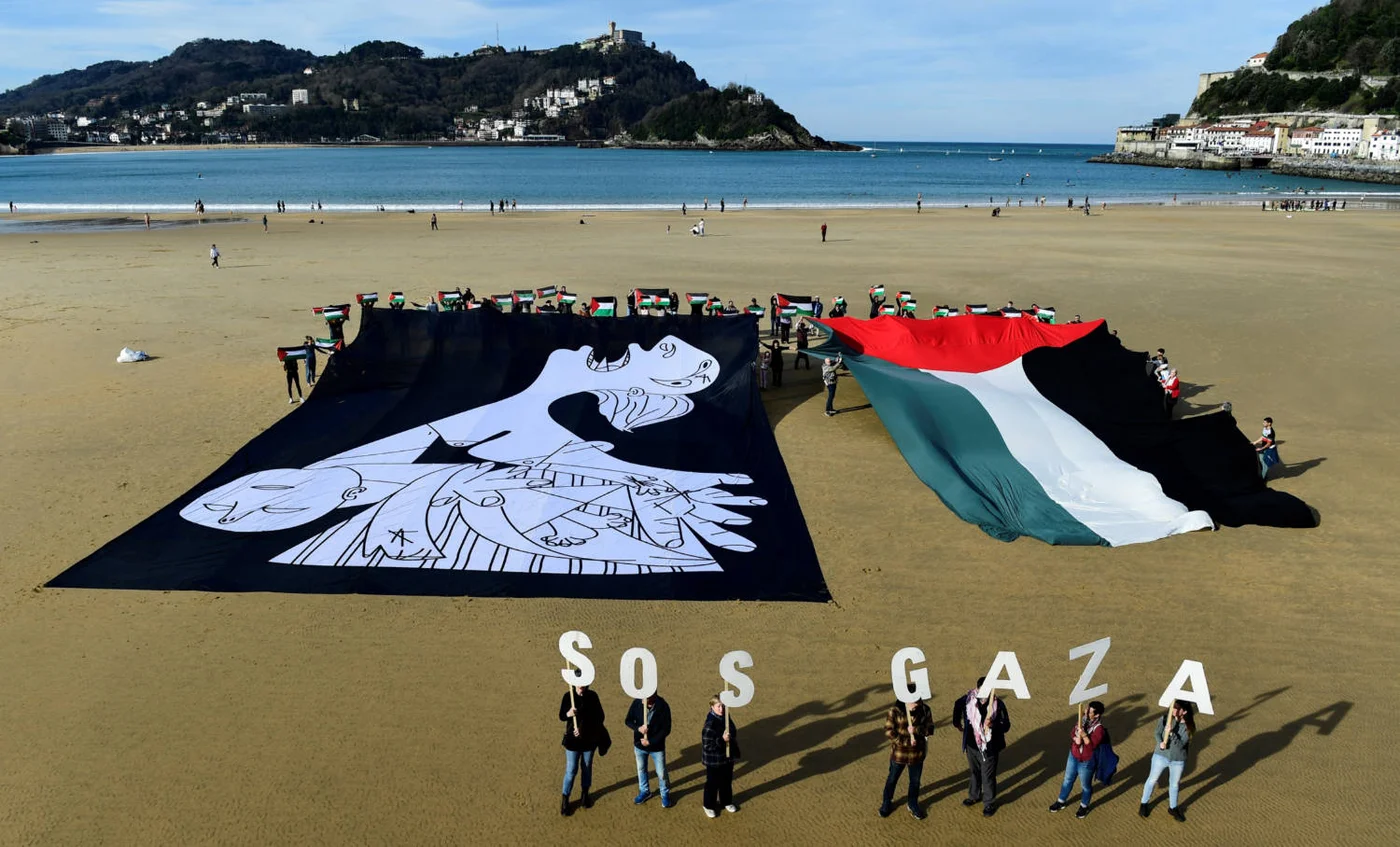 Demonstrators hold a canvas with a detail from Pablo Picasso's Guernica next to a giant Palestinian flag in San Sebastian, Spain, in January 2024 (AFP)