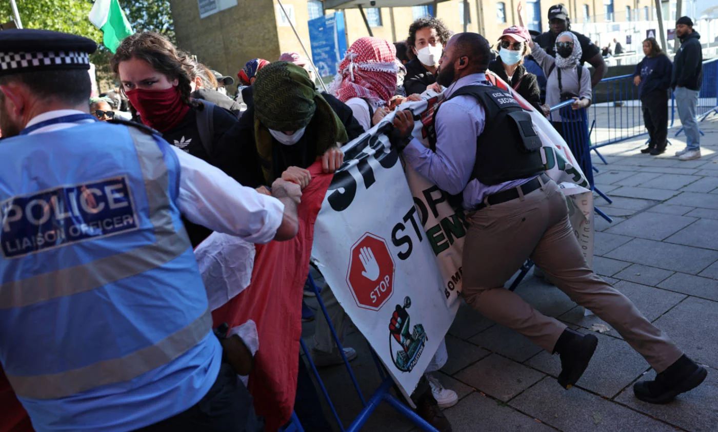 Demonstrators are held back by police and security outside the entrance to the DSEI  fair at the ExCeL centre, London, on 9 September 2025 (AFP)