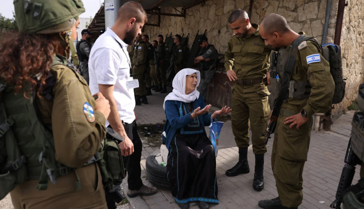 An elderly Palestinian woman in a wheelchair talks to Israeli forces at an army checkpoint in Bethlehem, occupied West Bank, on 28 March 2025 (AFP)