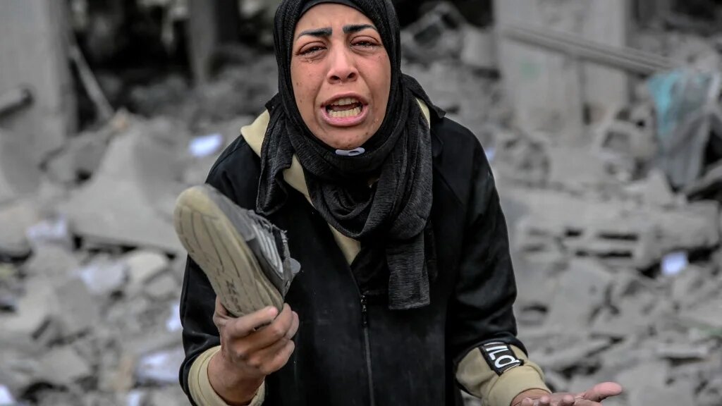 A Palestinian woman reacts as she holds her belongings next to the rubble of a building, after it was destroyed in an Israeli strike the night before, in the Rimal neighbourhood of Gaza City on March 16, 2024