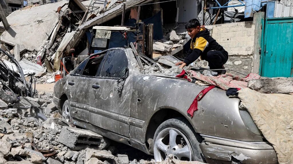 A boy clears rubble from atop a heavily damaged vehicle outside a destroyed building in Rafah in the southern Gaza Strip on April 5, 2024 amid the ongoing conflict in the Palestinian territory between Israel and the militant group Hamas. MOHAMMED ABED/AFP