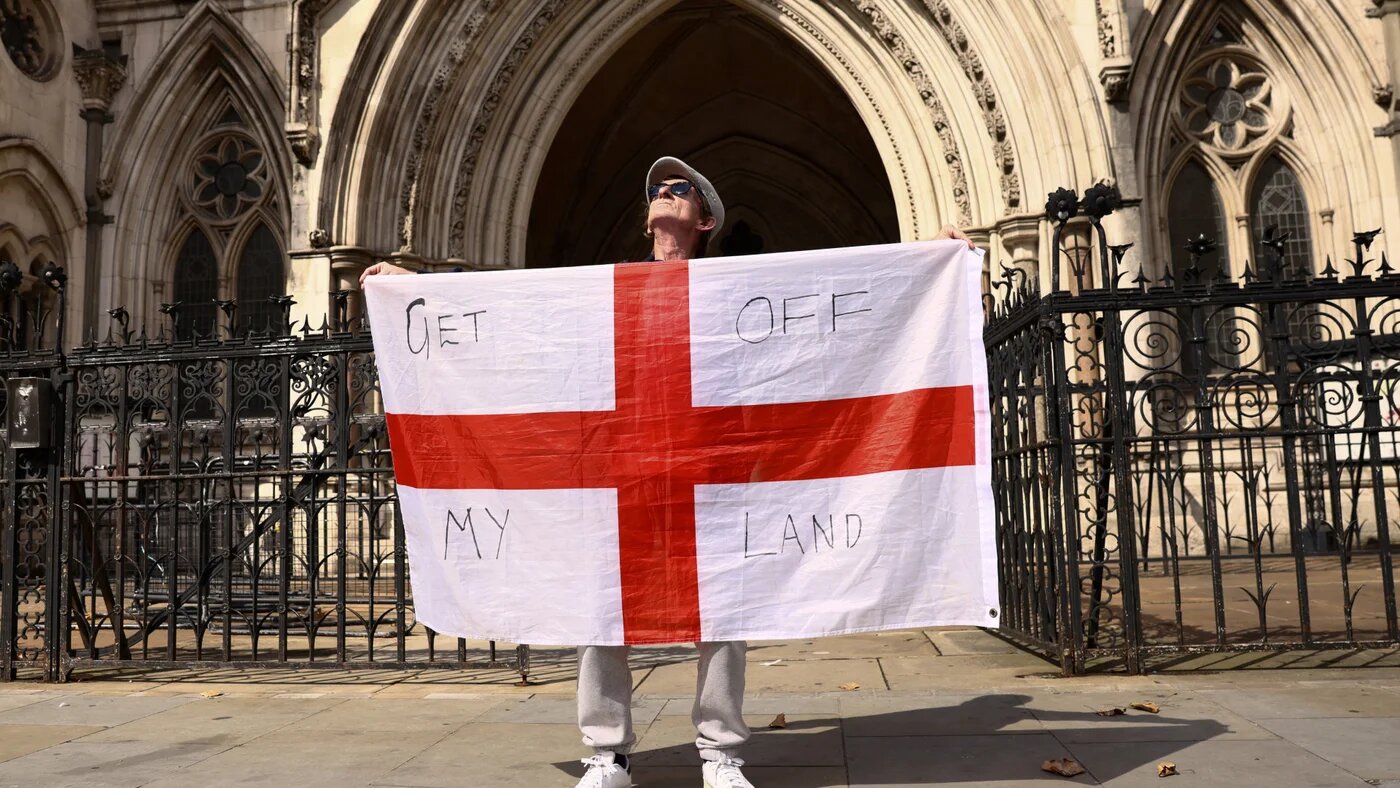A protester holds England’s St George’s flag outside the Royal Courts of Justice in London as the Court of Appeal rules on migrant removals, 29 August 2025 (Reuters/Jack Taylor)