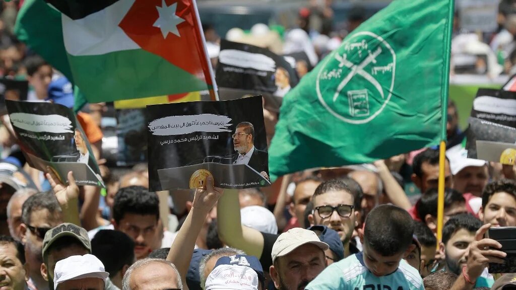 Le drapeau de la Jordanie (à gauche) et des Frères musulmans (à droite) apparaissent à côté d’une pancarte en l’honneur du président égyptien déchu, Mohamed Morsi, lors d’une manifestation à Amman, le 21 juin 2019, contre l’« accord du siècle » de Donald Trump (AFP)