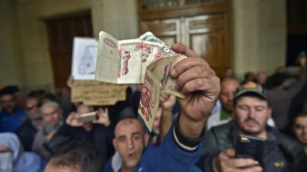 Un Algérien agite des billets de banque alors qu’une foule attend à l’entrée du tribunal, à Alger le 2 décembre 2019, avant l’ouverture d’un procès pour corruption d’anciennes personnalités politiques et économiques (AFP)