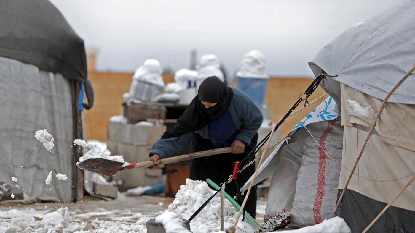 A woman who fled pro-regime forces attacks in northeastern Syria, clears the snow in front of a tent at camp for displaced people in the northern Syrian town of Tal Abyad by the border with Turkey, on February 13, 2020. (Bakr ALKASEM/AFP)