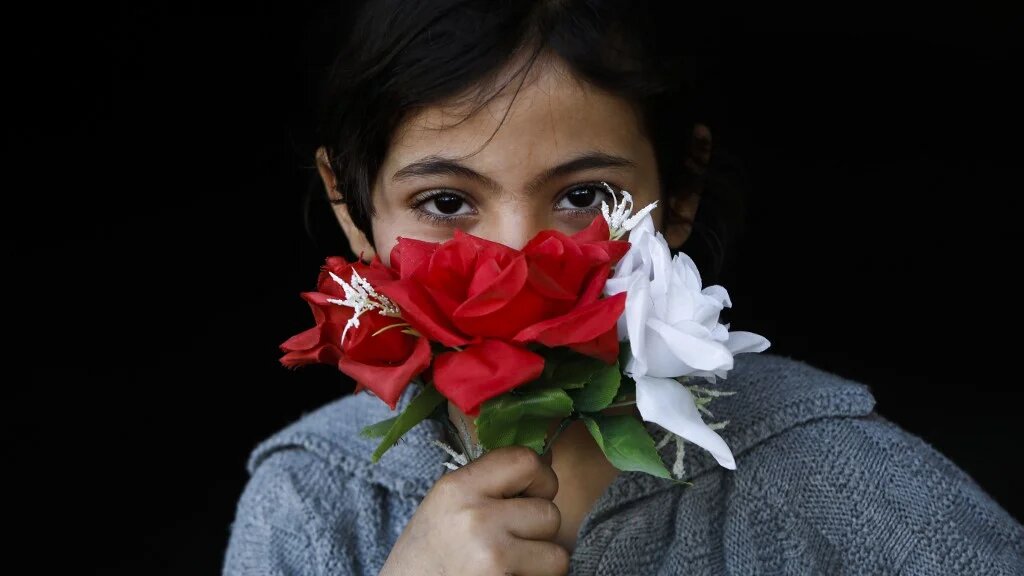 Une fillette palestinienne couvre sa bouche avec des fleurs en guise de masque, à Beit Lahia, au nord de Gaza, le 16 avril 2020 (AFP)