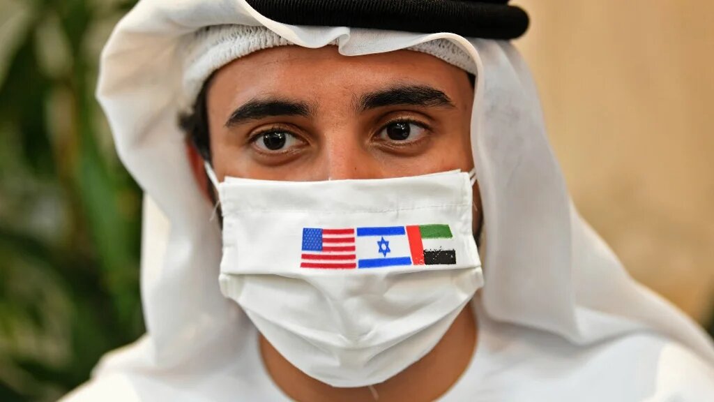 Une photo prise le 31 août 2020 montre un Émirati portant un masque de protection avec les drapeaux des États-Unis, d’Israël et des Émirats arabes unis avant l’arrivée du premier vol commercial en provenance d’Israël (AFP)