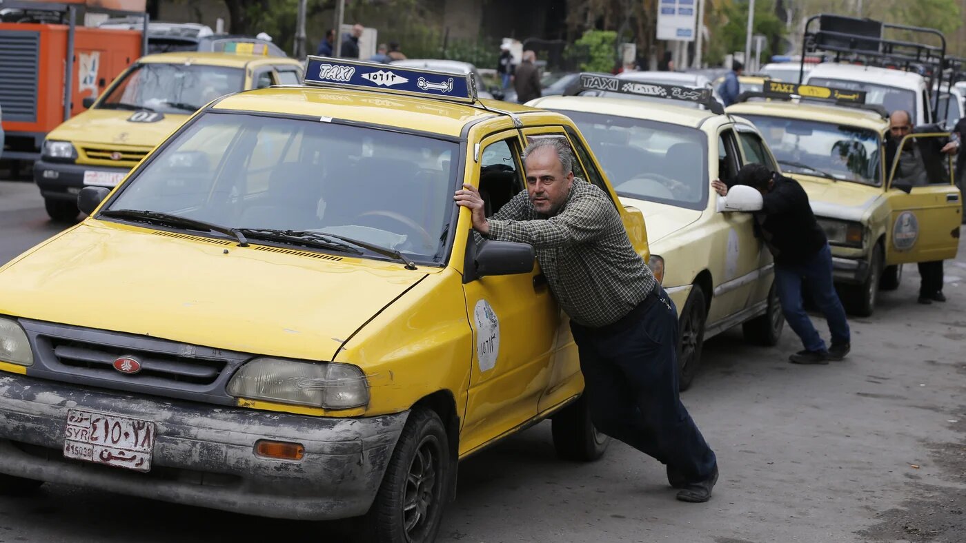Taxi drivers push their cars that ran out of gasoline to a petrol station in the Syrian capital Damascus on April 16, 2019.