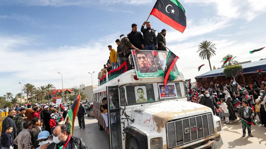 Les gens brandissent des drapeaux nationaux libyens dans la ville côtière de Tadjourah, à l’est de la capitale Tripoli, le 25 février 2022 (AFP/Mahmoud Turkia)
