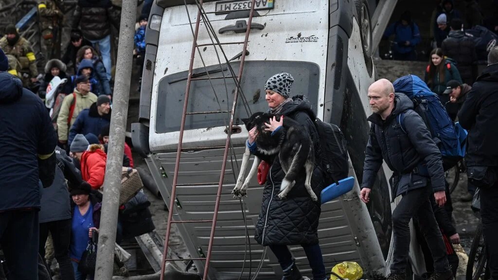 Une femme porte son chien tandis que des personnes traversent un pont détruit pendant l’évacuation de la ville d’Irpin, au nord-ouest de Kiev, lors de bombardements, le 5 mars 2022 (AFP/Aris Messinis)
