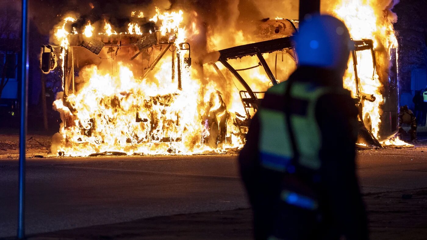 An anti-riot police officer watches a city bus burning in Malmo on 16 April 2022 (AFP)