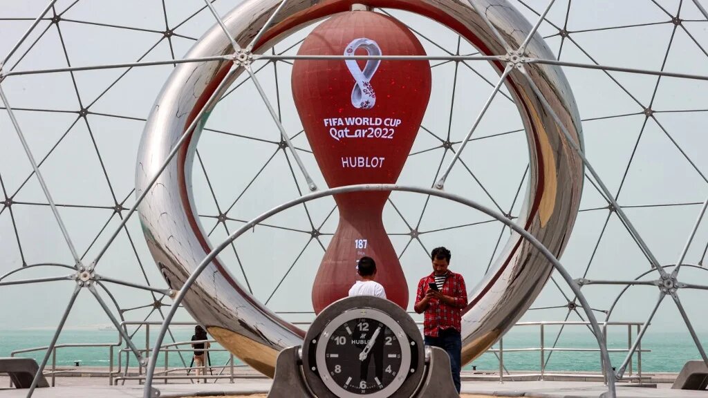 People stand by the clock installation ticking the days to the start of the Qatar 2022 FIFA World Cup, along the waterfront in Qatar's capital Doha during a heavy dust storm on May 17, 2022 as the skyline behind is obscured in the haze. (AFP)