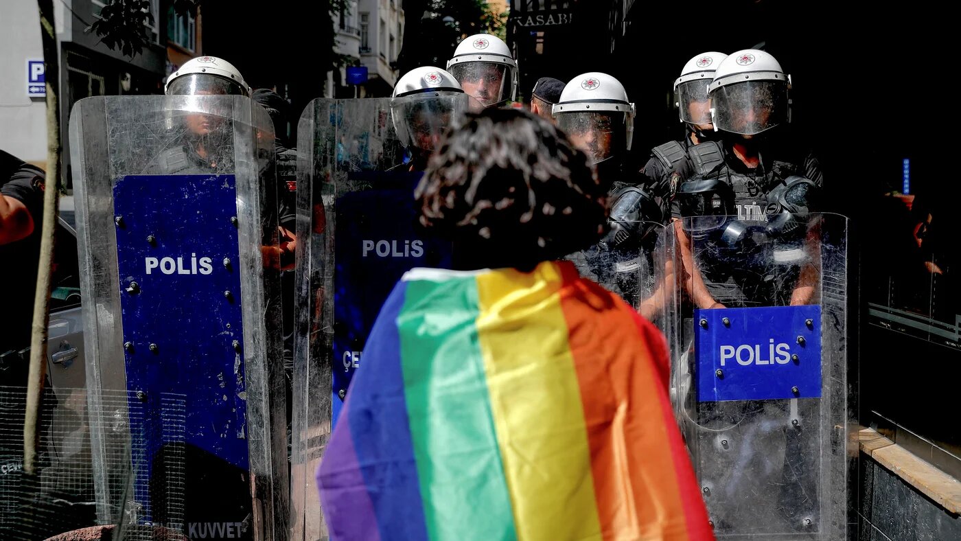 A participant faces riot policemen wearing a rainbow flag during a Pride march in Istanbul, on June 26, 2022. (AFP)
