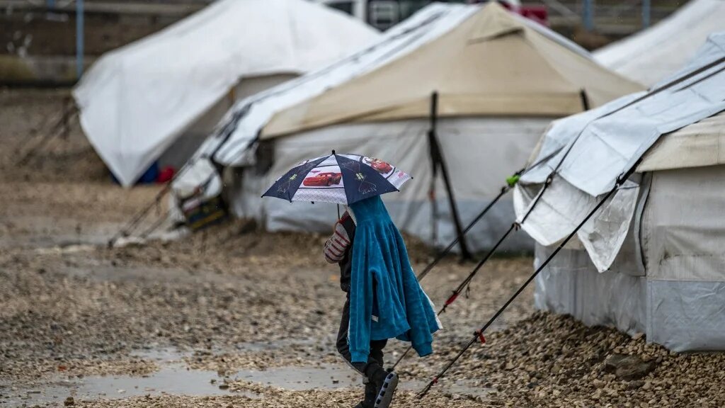 Un enfant marche sous la pluie au Camp de Roj, où sont détenus des proches de personnes soupçonnées d’appartenir au groupe État islamique (EI), dans le nord-est de la Syrie (AFP/Delil Souleiman) 