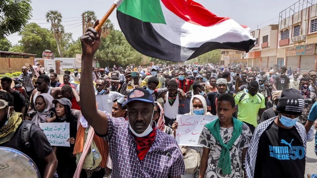 An anti-coup protester waves a Sudanese national flag while marching with others during mass demonstrations against military rule in the centre of Sudan's capital Khartoum on June 30, 2022 (AFP)
